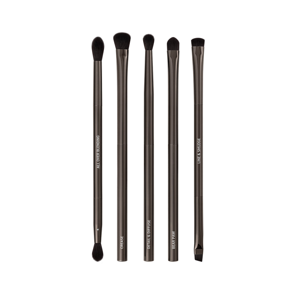 Makeup brush set with six dark bristles and sleek gray metallic handles, upright.