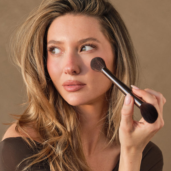 Powder brush applying makeup with soft black bristles and metallic handle
