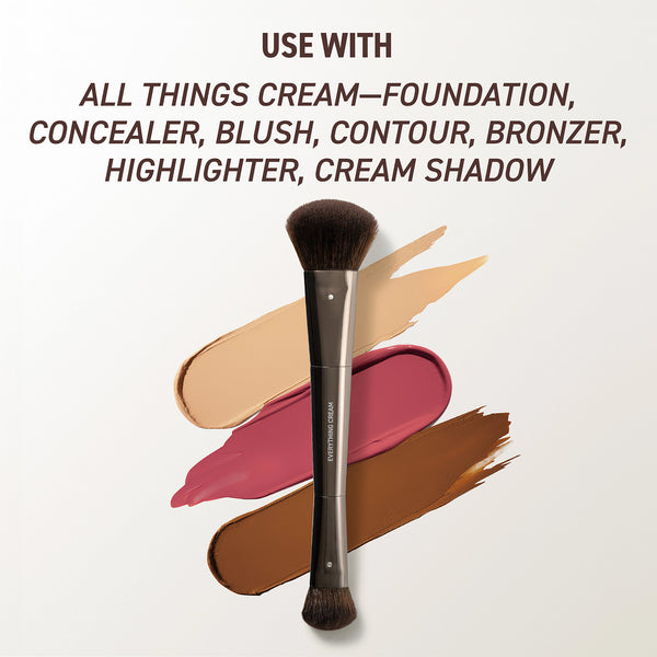 Makeup brush with black bristles shown over cream foundation and blush swatches.