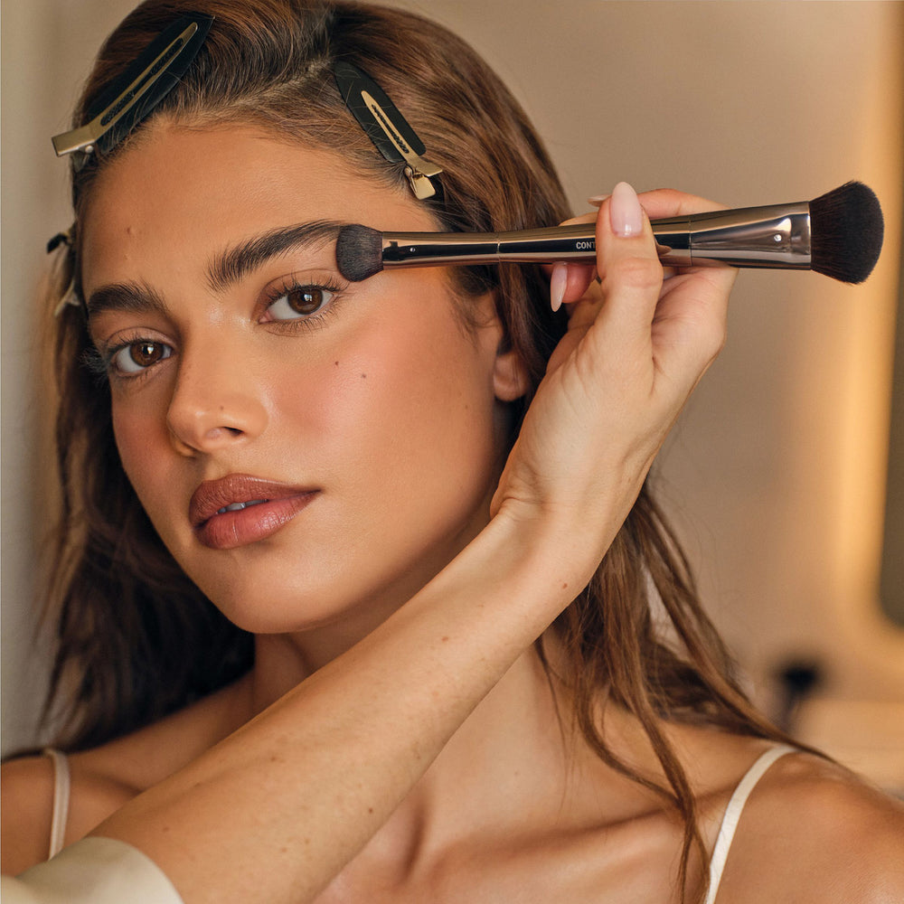 Makeup brush with short black bristles and a dark straight handle.